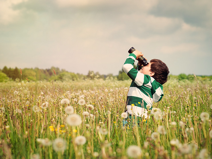 Little boy using binoculars outside to observe nature