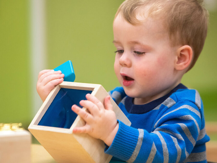 Toddler playing with wooden box at Bright Horizons day care 