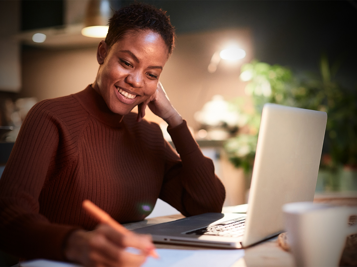 woman at her desk working on laptop and taking notes smiling