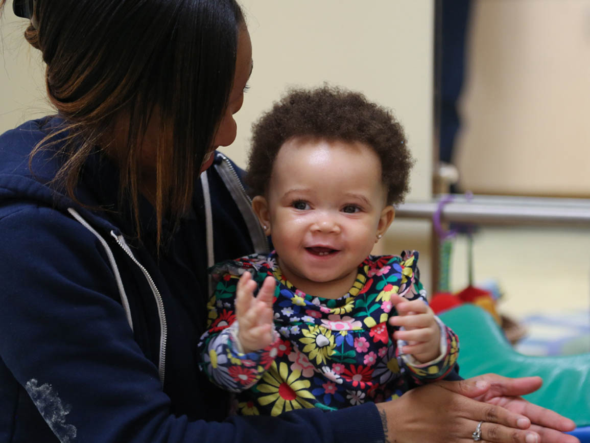 Clapping baby girl sitting on teacher's lap