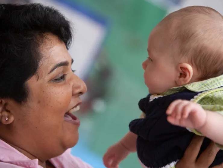 Teacher smiles and speaks parentese to a baby at daycare