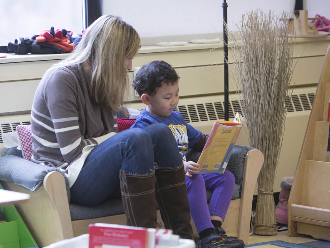 Preschool boy reading a book with a teacher