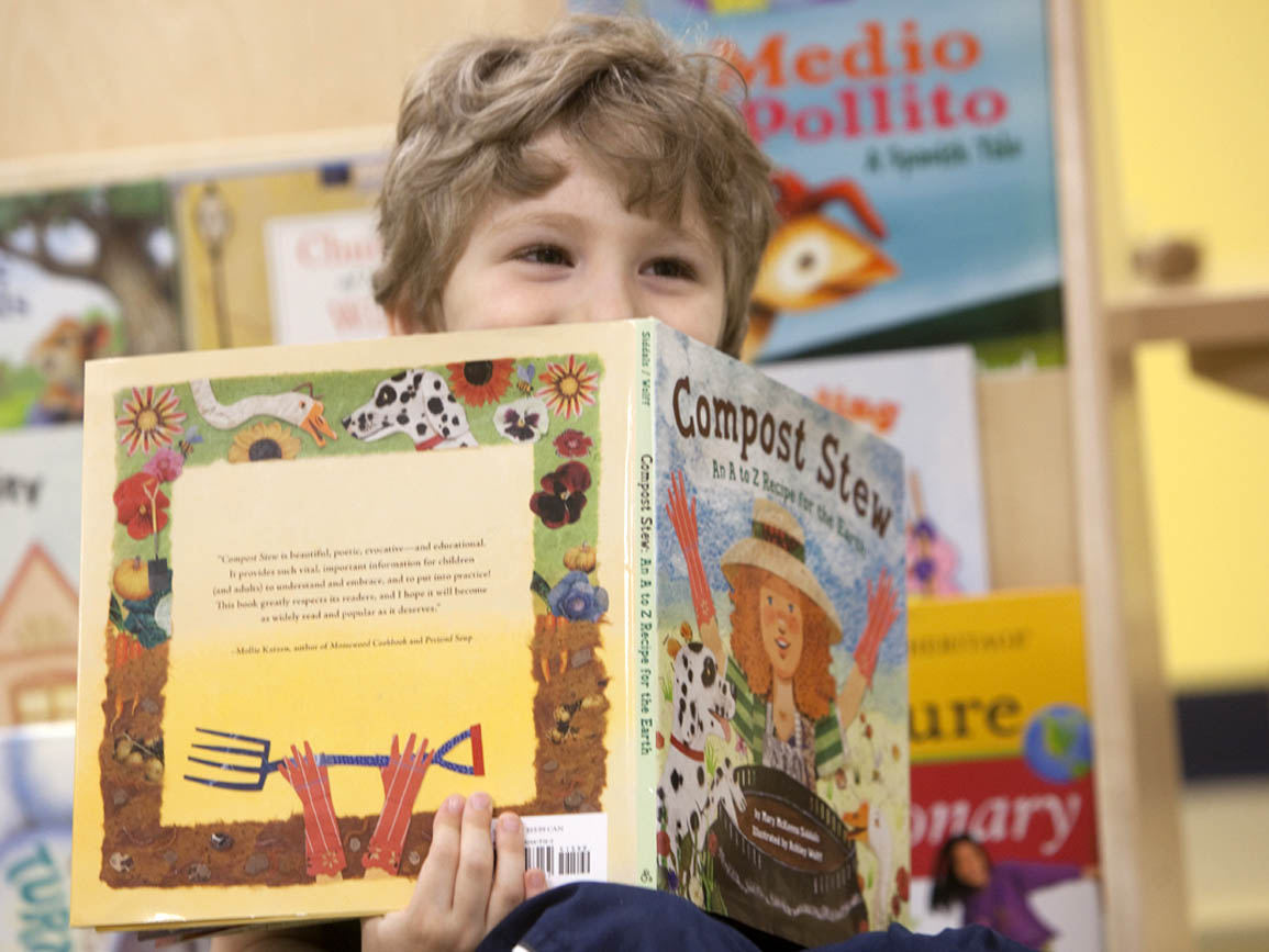 Young boy smiling and holding up a book