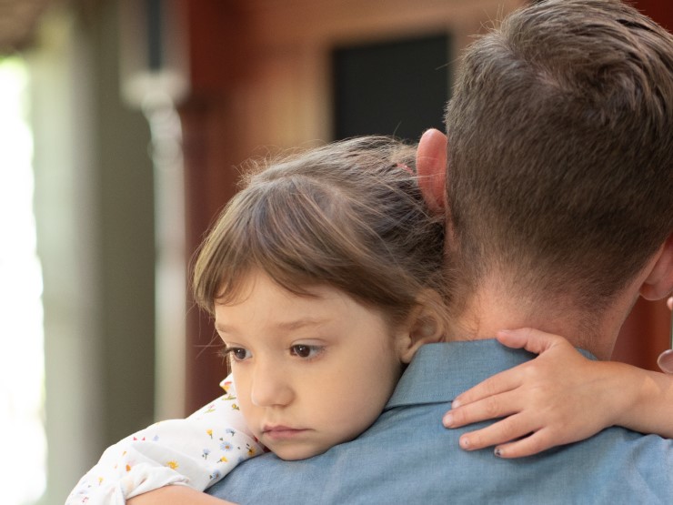 Father reassuringly holds scared daughter at daycare